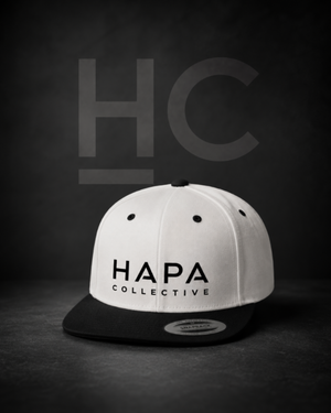 A structured snapback cap with a white crown and black flat brim, featuring the text 'HAPA COLLECTIVE' printed in black on the front. The cap is photographed on a dark, textured studio background with a faint 'HC' watermark behind it.